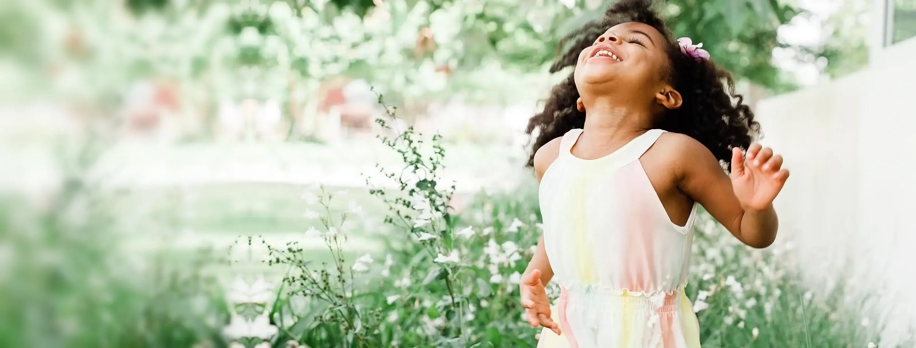 A young girl laughing with joy in a sunlit garden