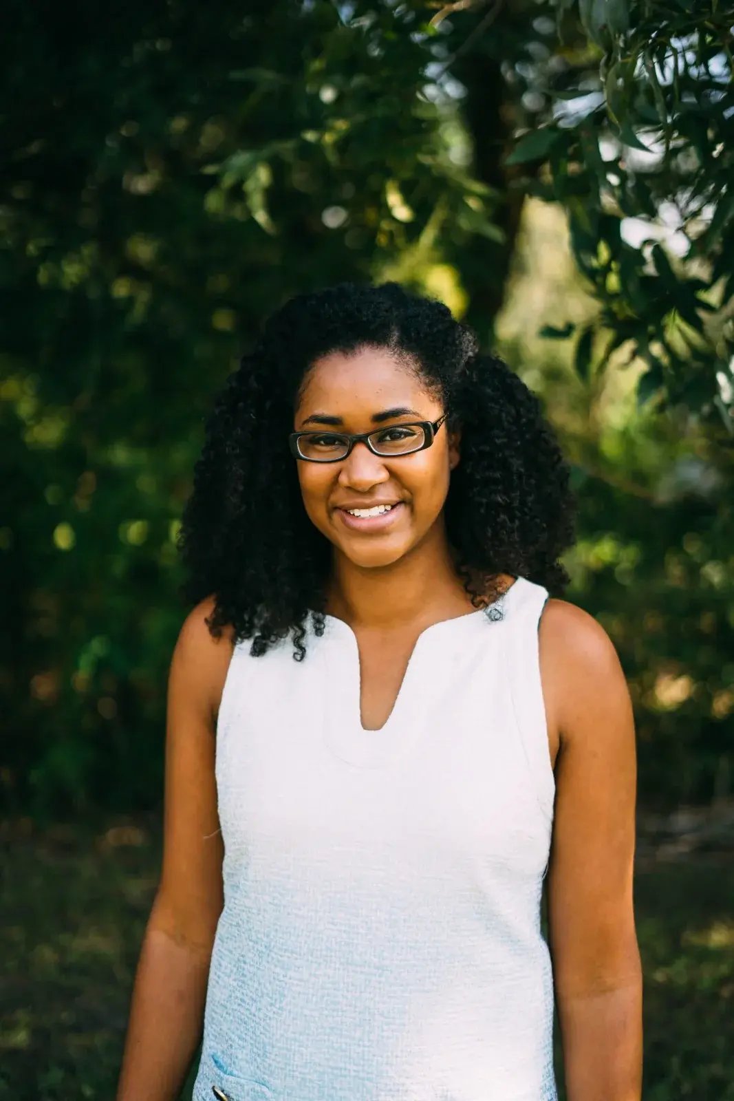 Dr. Allison J. McDade, MD, smiling in glasses in a sunlit garden